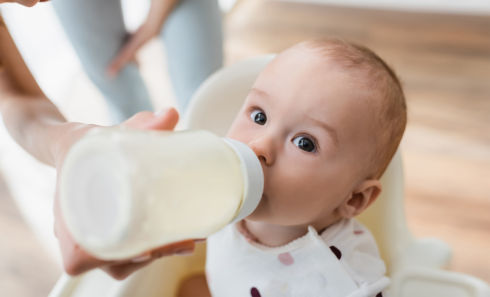 Dorosła osoba karmi siedzące niemowlę mlekiem z butelki