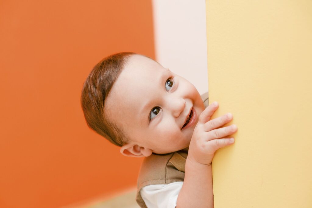 Mały, uśmiechnięty chłopiec wygląda zza żółtej ściany.